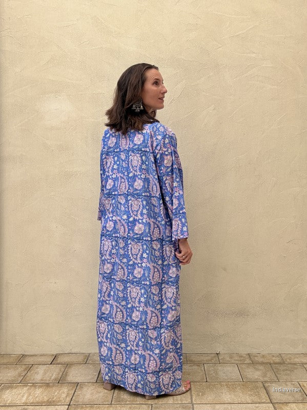 Woman wearing a blue patterned dress standing against a beige wall.