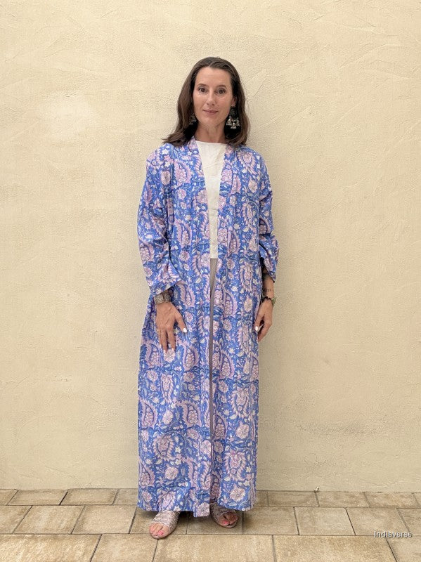 woman wearing a blue and pink paisley printed long abaya robe standing against a beige wall