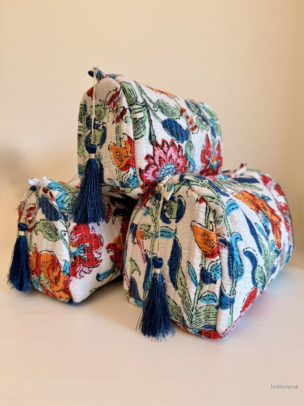 Three small drawstring cosmetic pouches with navy blue tassels, featuring a colorful floral and botanical print on a cream background, arranged on a light beige surface against a solid beige background | Flower Bouquet