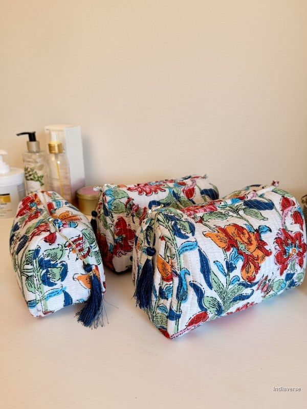 Three fabric cosmetic pouches with a colorful floral and bird print in red, blue, green, and orange on a white background, with dark blue tassels, arranged on a beige surface against a beige wall | Flower Bouquet