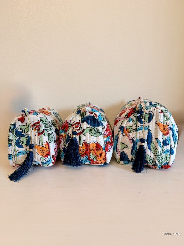 Three small drawstring pouches with navy blue tassels, featuring a colorful bird and floral print on a white background, arranged in a row against a plain beige wall | Flower Bouquet