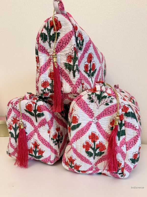 Three small quilted fabric pouches with pink and white floral patterns and red tassels, arranged together on a light surface against a plain beige wall | Flower Candy
