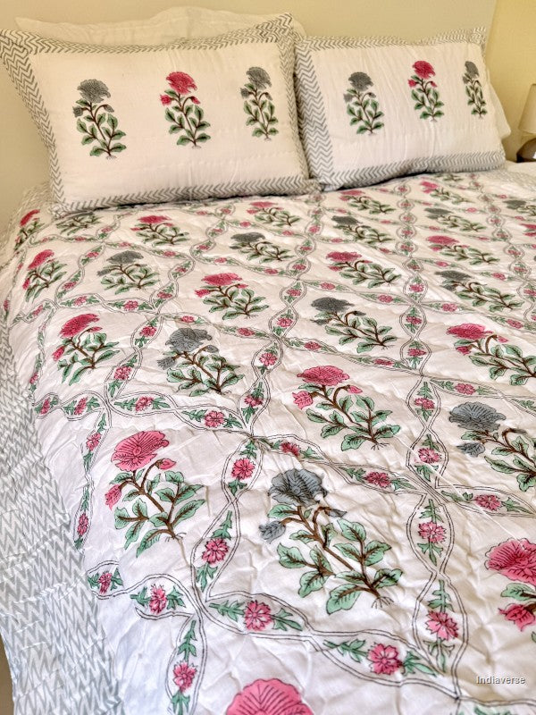 A quilted blanket with red and blue flower design arrange in a geometric pattern on a white double bed in a bedroom and with two matching pillowcases