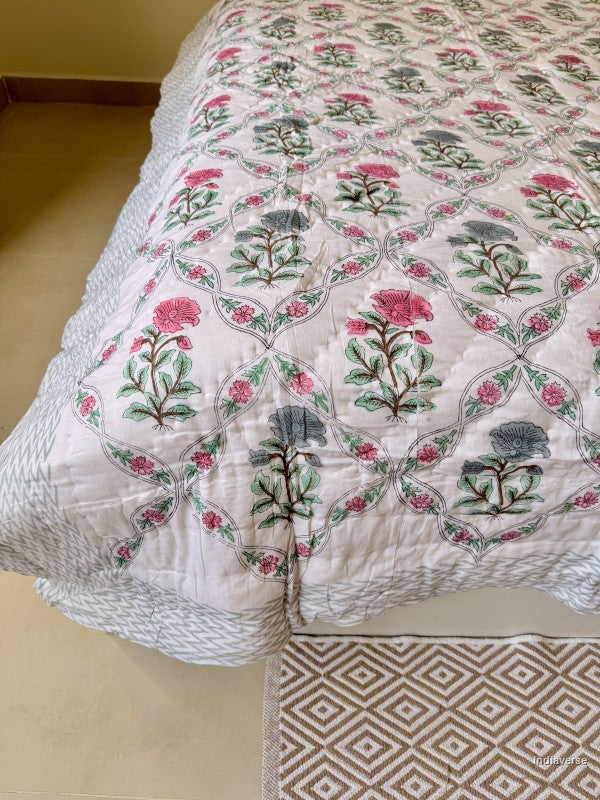 Close up of the edge of a quilted blanket with red and blue flower design arrange in a geometric pattern thrown across a bed