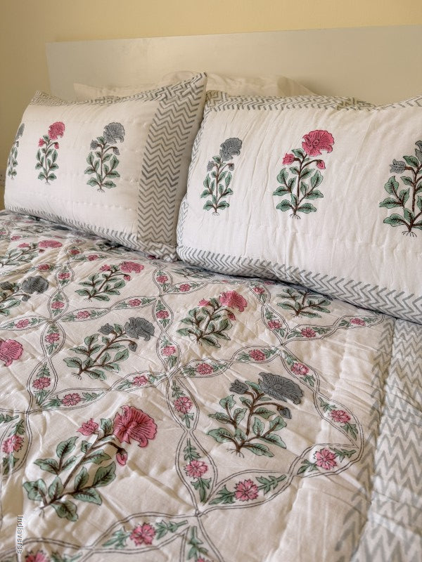 Close up of two quilted pillowcases with floral print arranged on a quilted blanket with red and blue flower design arrange in a geometric pattern