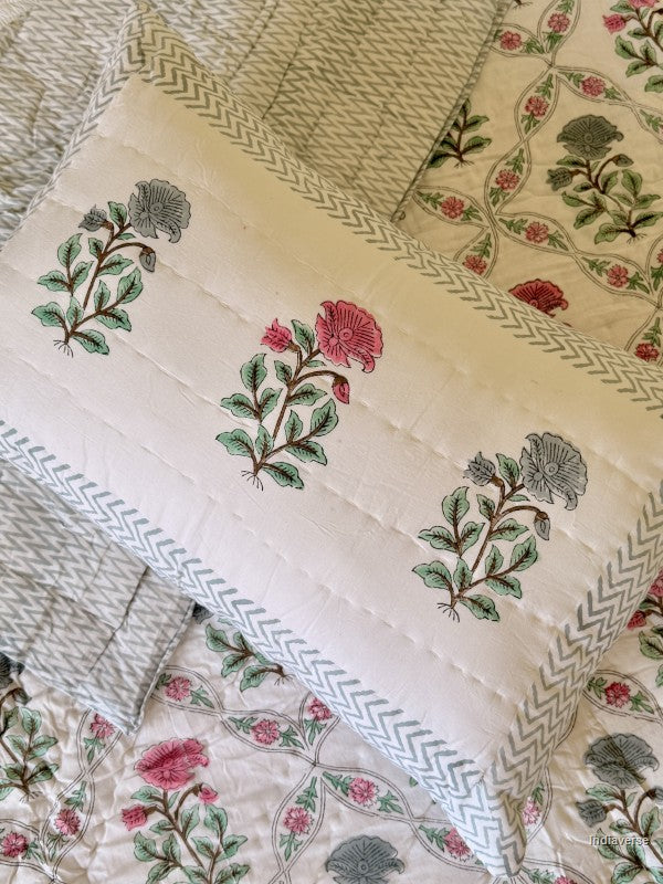 Close up of a pillowcase with single flowers in red and blue printed on it arranged on a quilted blanket with red and blue flower design arrange in a geometric pattern