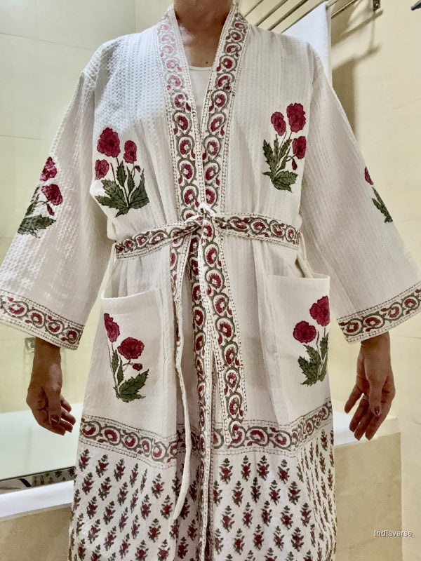 A white cotton kimono-style robe with red and green floral embroidery and patterned borders, worn by a person in a bathroom setting.