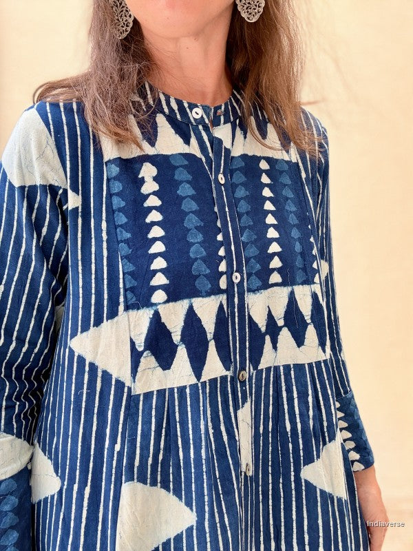 A close-up of a woman wearing a long-sleeve button-front tunic top with a blue and off-white geometric patchwork pattern, set against a plain beige background.