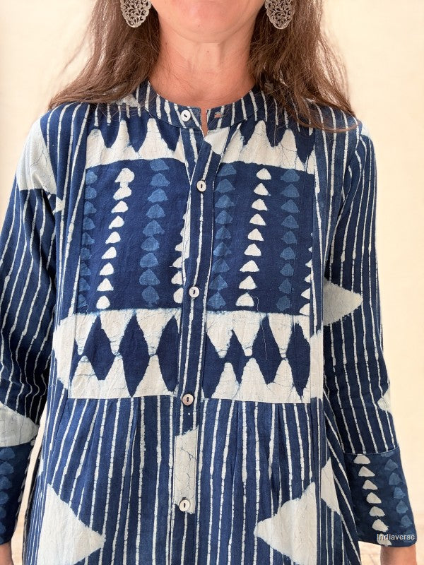 A close-up of a person wearing a long-sleeve button-front top with a bold blue and white geometric patchwork pattern, including stripes, triangles, and diamond motifs.