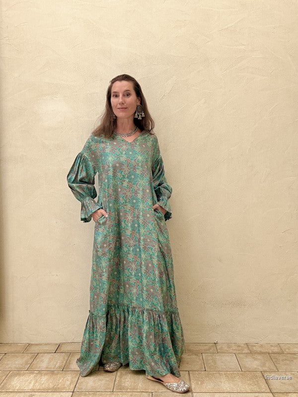 Woman wearing a green patterned dress standing against a beige wall.