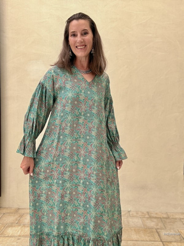 Woman wearing a green patterned dress standing against a beige wall.