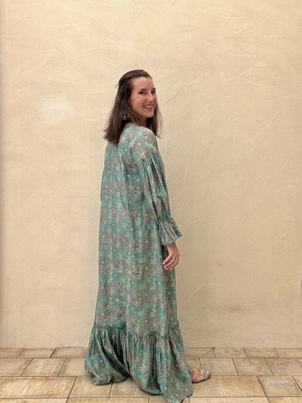 Woman wearing a green floral dress standing against a beige wall.