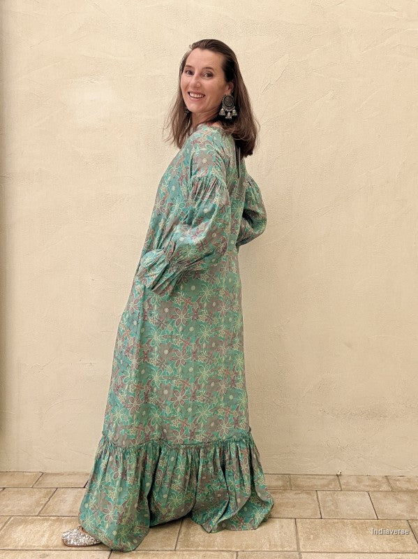 Woman wearing a long green floral dress against a beige wall.