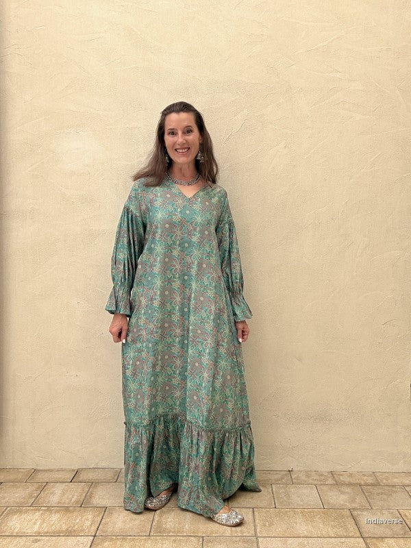 Woman wearing a green patterned dress standing against a beige wall.