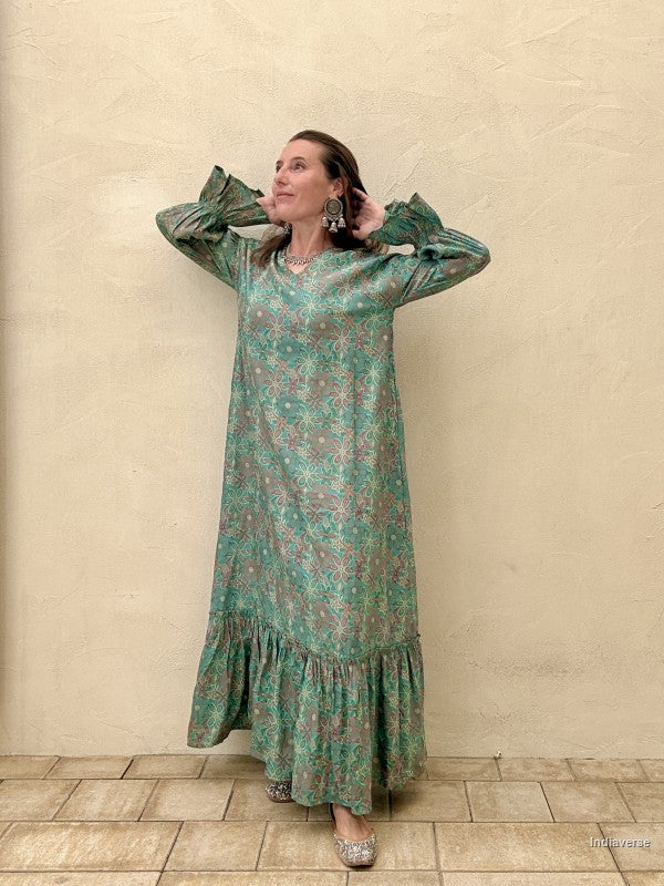 Woman wearing a green patterned dress against a beige wall.