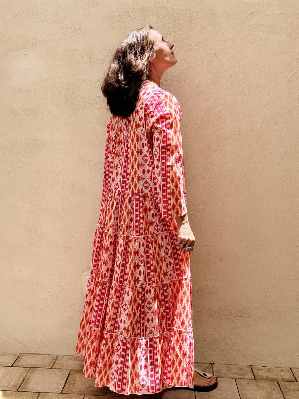 Woman wearing a long, patterned dress against a beige wall.