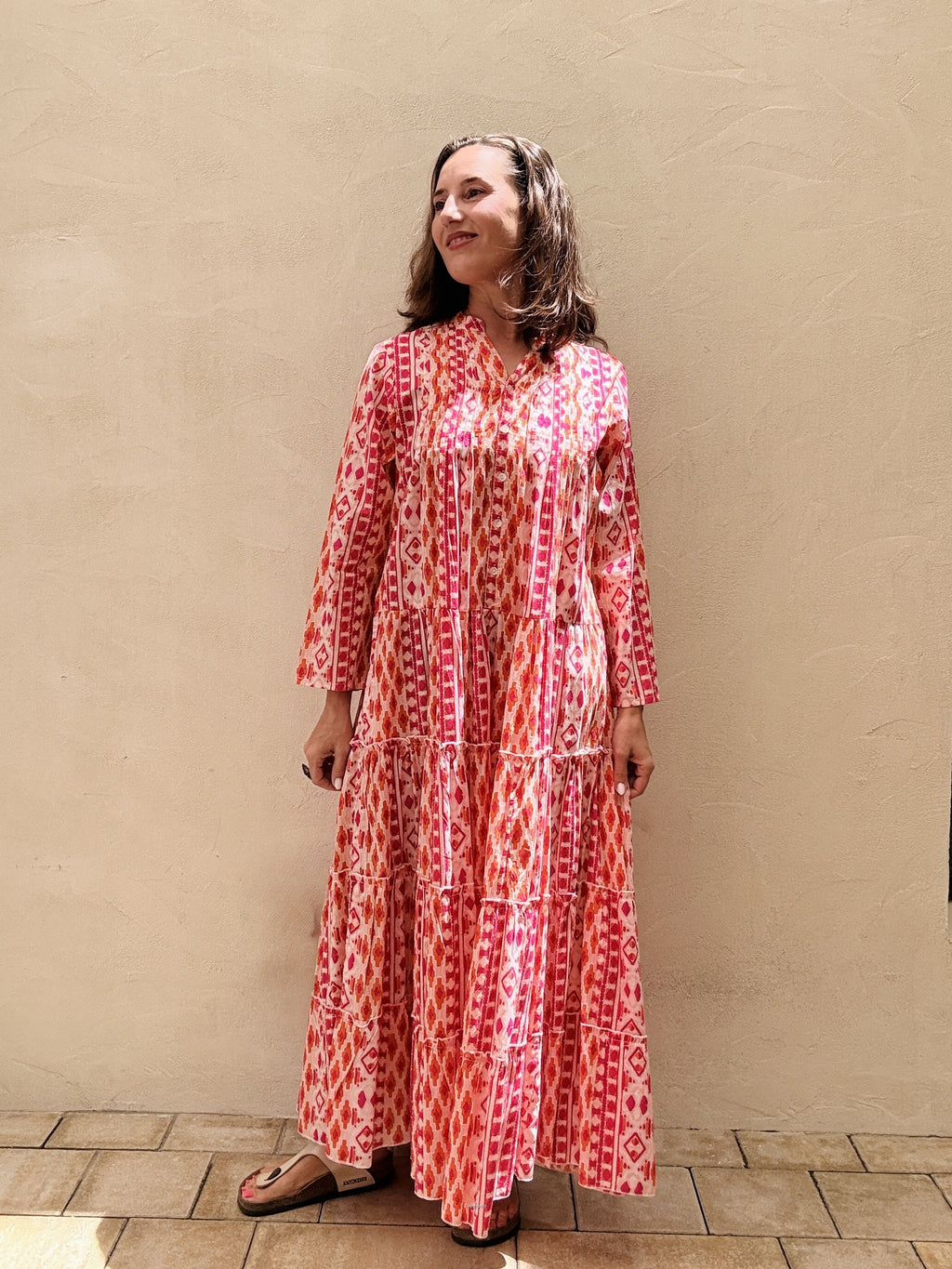 Woman wearing a red and white patterned dress standing against a beige wall.