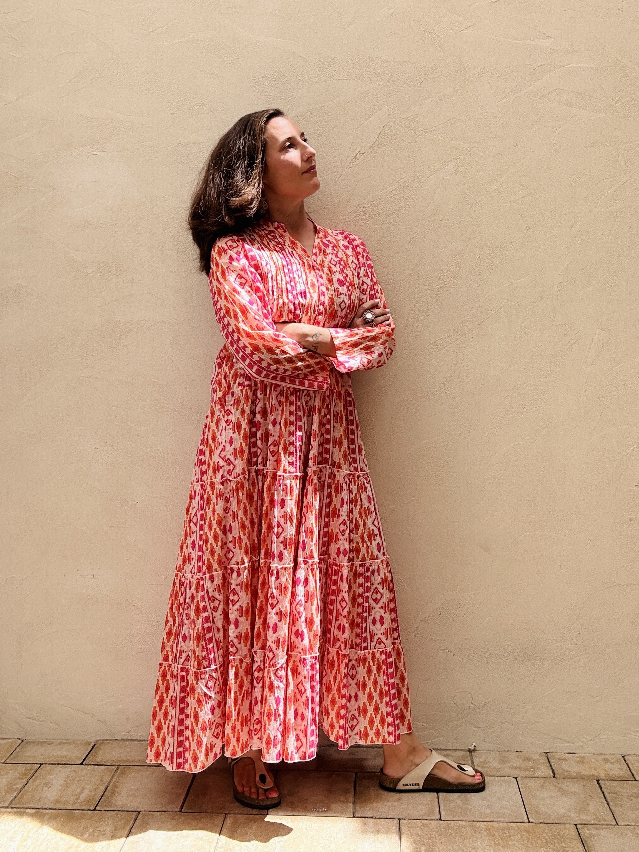 Woman in a red patterned dress standing against a beige wall.