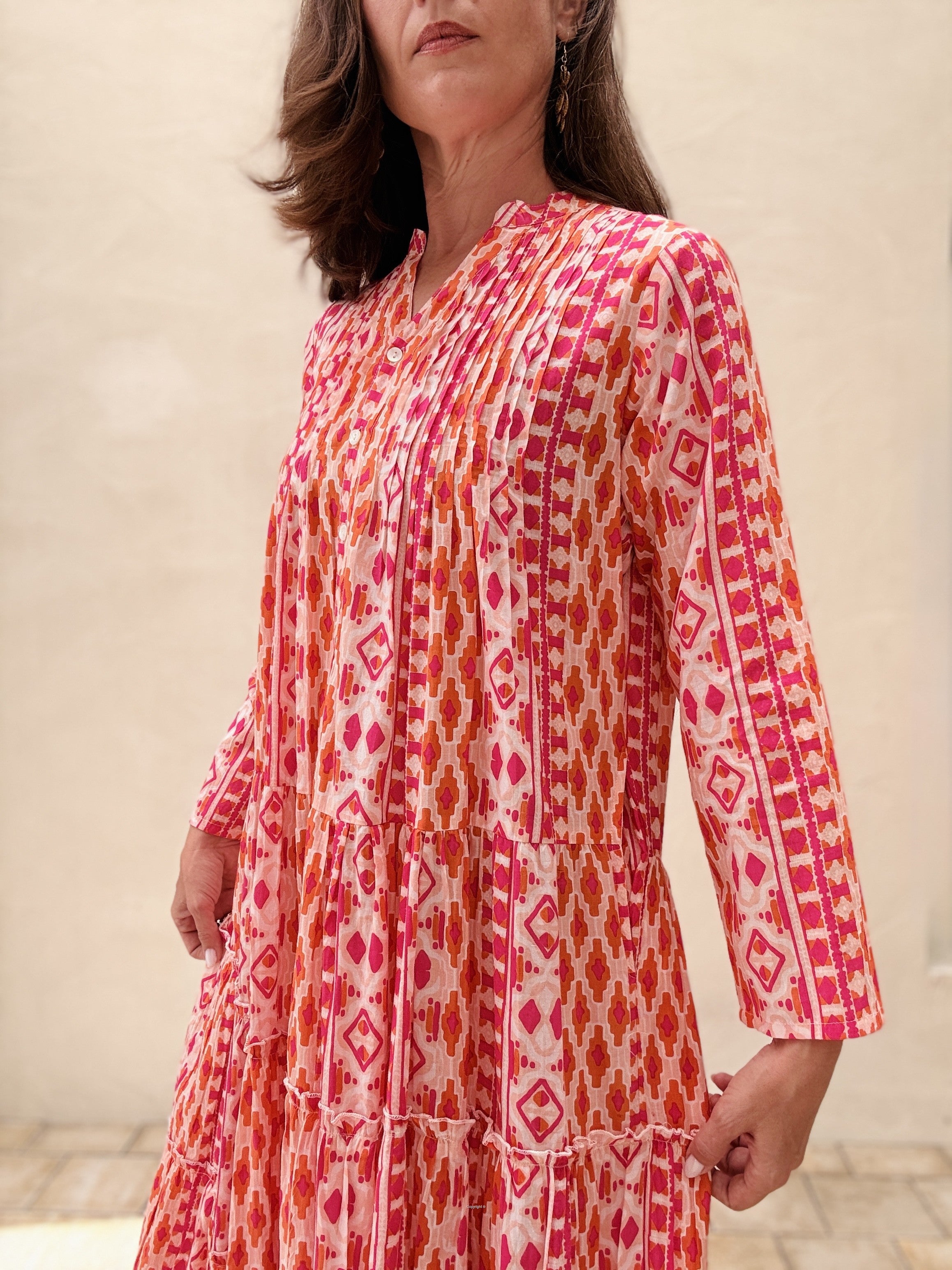 Woman wearing a red and orange patterned dress against a neutral background
