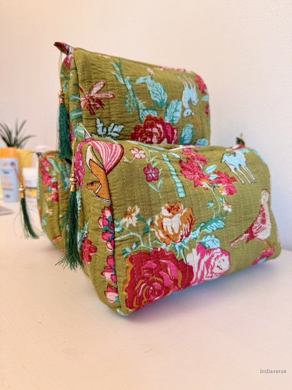 A set of three quilted fabric cosmetic pouches in a green base color with a colorful floral and animal print, featuring dark green tassels, displayed on a light beige surface against a neutral background | Magic Garden