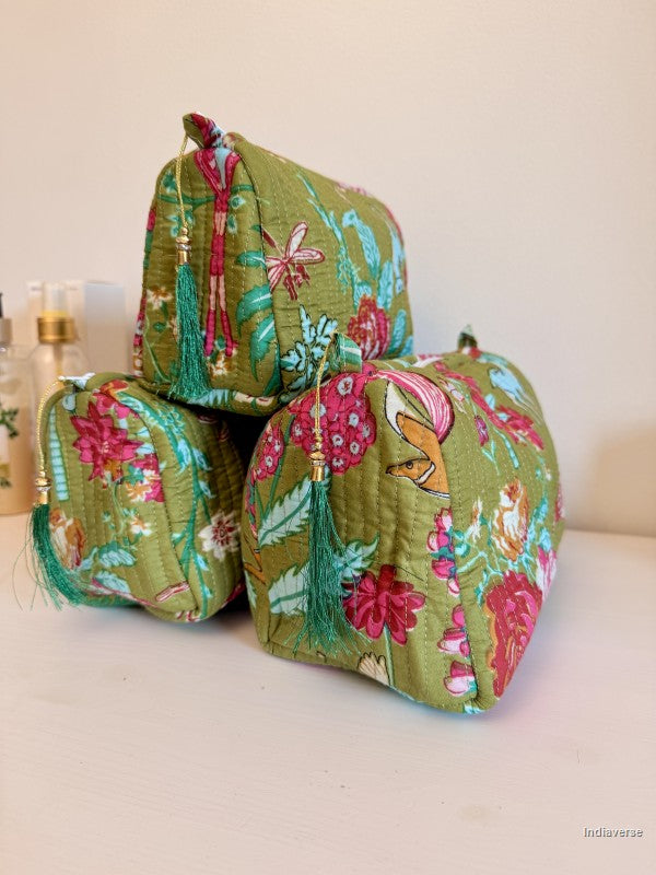 Three small quilted cosmetic pouches in olive green fabric with a colorful floral and butterfly print, decorated with tassel ties, arranged on a light surface against a plain beige background | Magic Garden