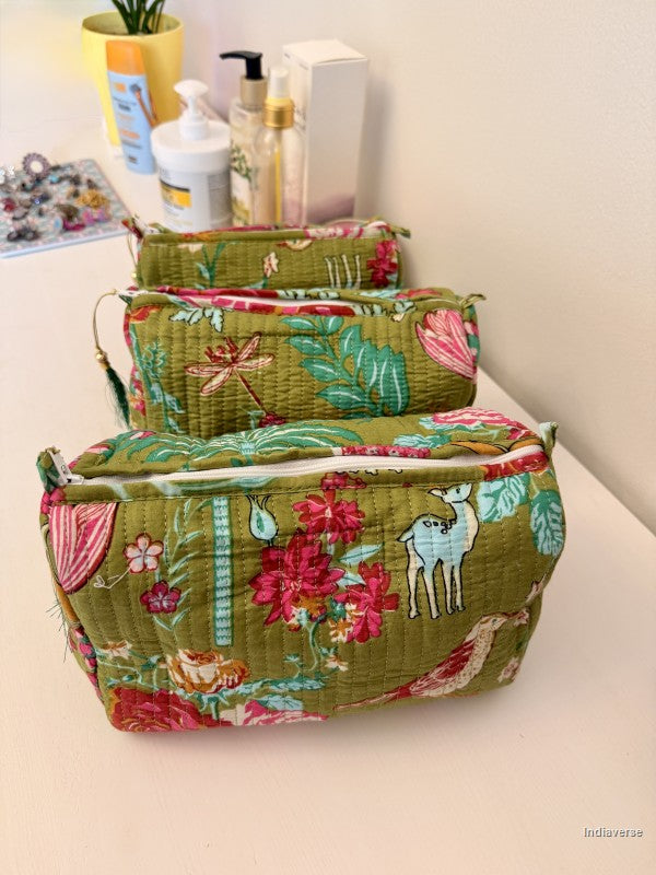 Three quilted fabric zippered pouches in a matching green floral and nature print, arranged by size on a light beige surface with cosmetic bottles in the background | Magic Garden