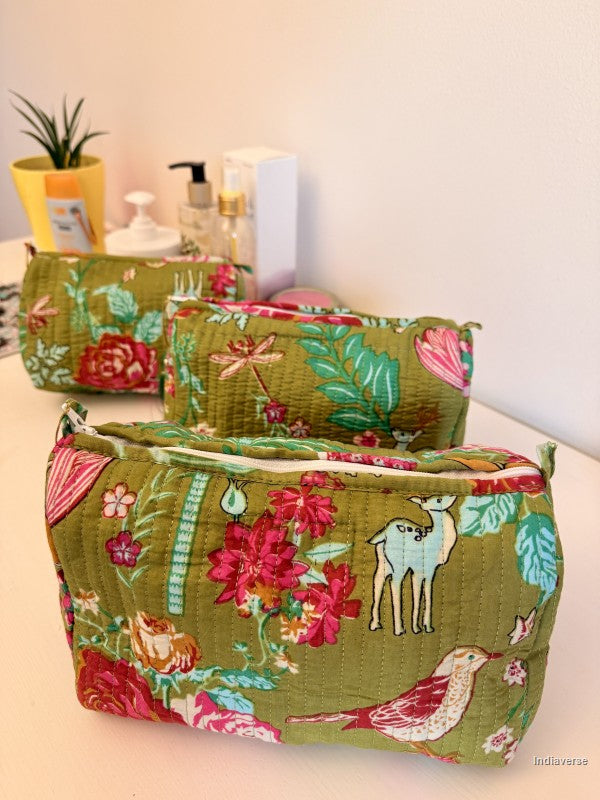 Three quilted fabric cosmetic pouches in a matching floral print, arranged on a light-colored tabletop with toiletry bottles and a small plant in the background | Magic Garden