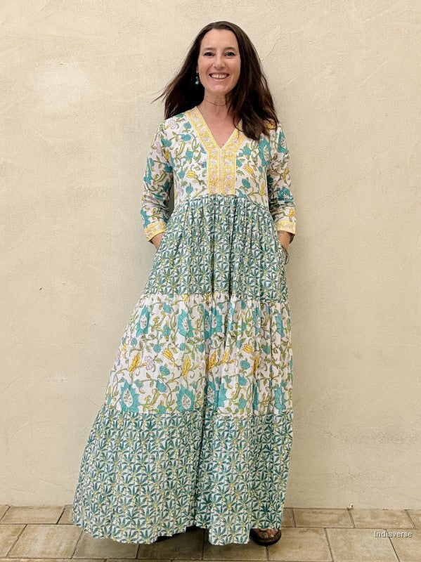 Woman wearing a long cotton dress with green palm tree motif and floral print standing against a beige wall
