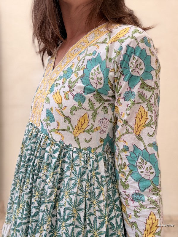 Close up of a woman wearing a long cotton dress with green palm tree motif and floral print standing against a beige wall