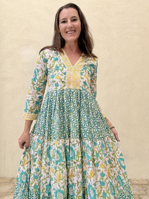 Woman wearing a long cotton dress with green palm tree motif and floral print standing against a beige wall