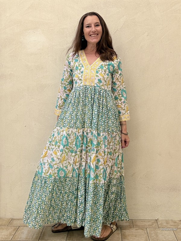 Woman wearing a long cotton dress with green palm tree motif and floral print standing against a beige wall