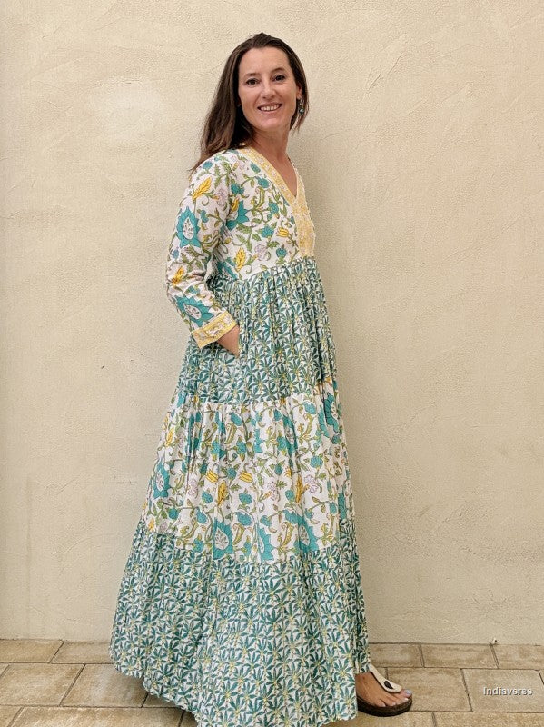 Woman wearing a long cotton dress with green palm tree motif and floral print standing against a beige wall