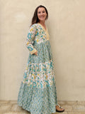 Woman wearing a long cotton dress with green palm tree motif and floral print standing against a beige wall