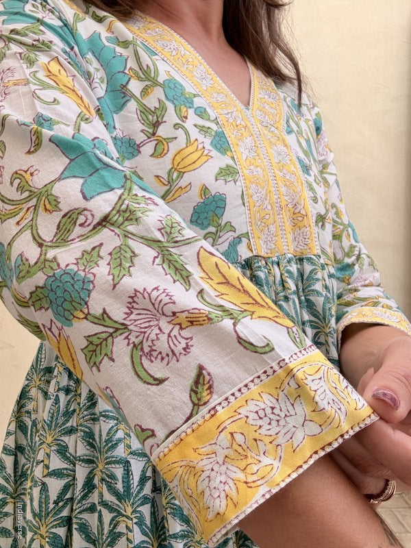 Close up of the dress sleeve worn by a woman wearing a long cotton dress with green palm tree motif and floral print standing against a beige wall