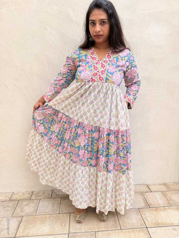 Woman wearing a floral dress with a white overlay on a tiled floor.