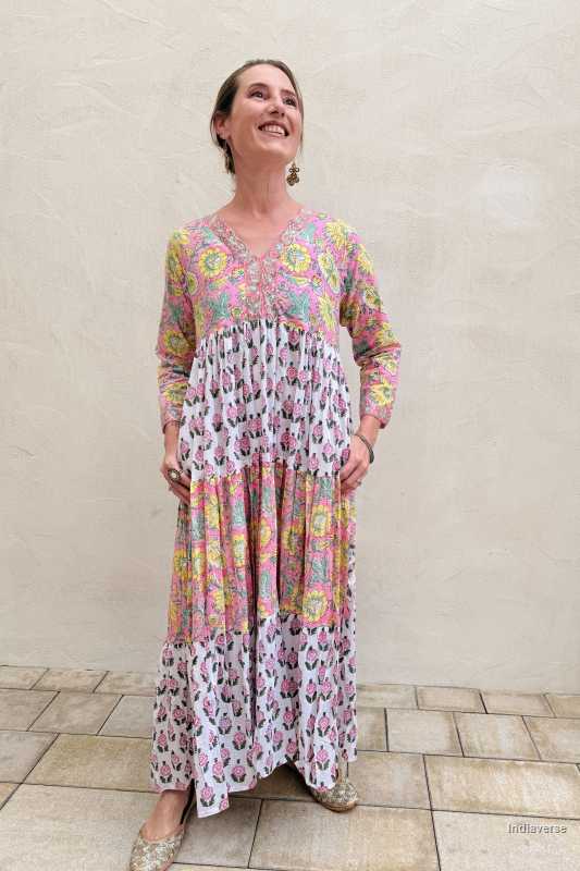 Woman wearing a colorful patterned dress standing against a plain wall.