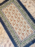 A rectangular area rug with a cream center field featuring a dense floral pattern in rust orange and sage green, surrounded by a navy blue border with geometric patterns.
