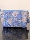 Blue floral-patterned pouch with tassels on a reflective surface