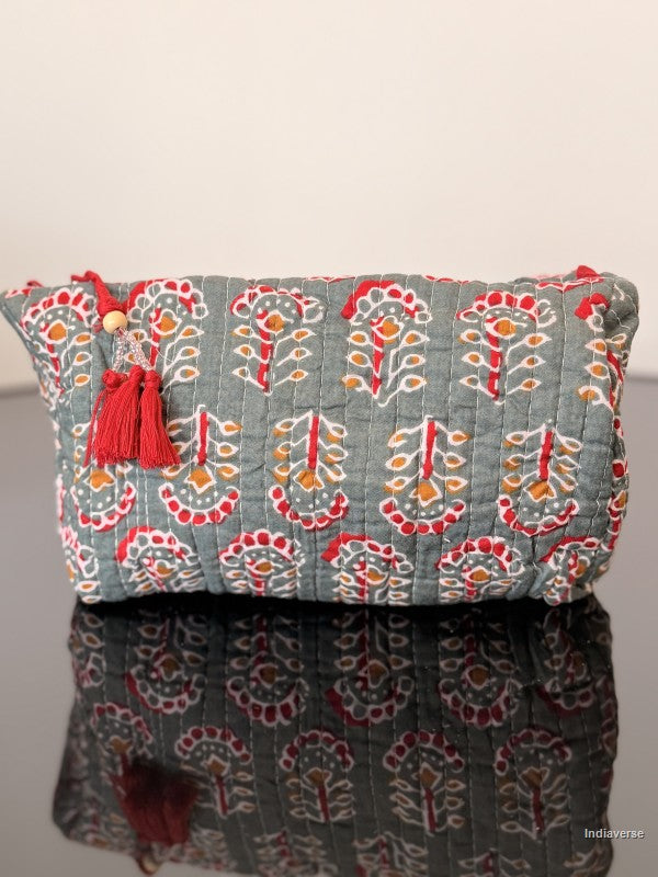 Decorative clutch bag with floral pattern and red tassels on a reflective surface.