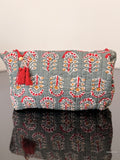 Decorative clutch bag with floral pattern and red tassels on a reflective surface.