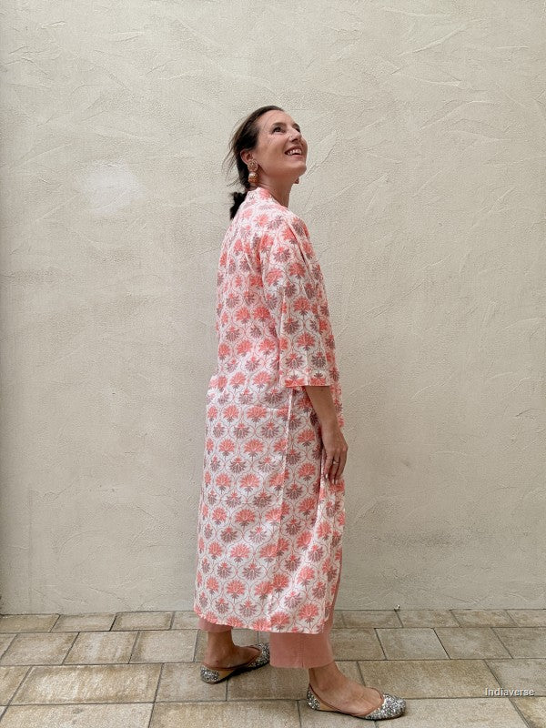 woman wearing a midi size kimono with orange lotus print standing against a beige wall