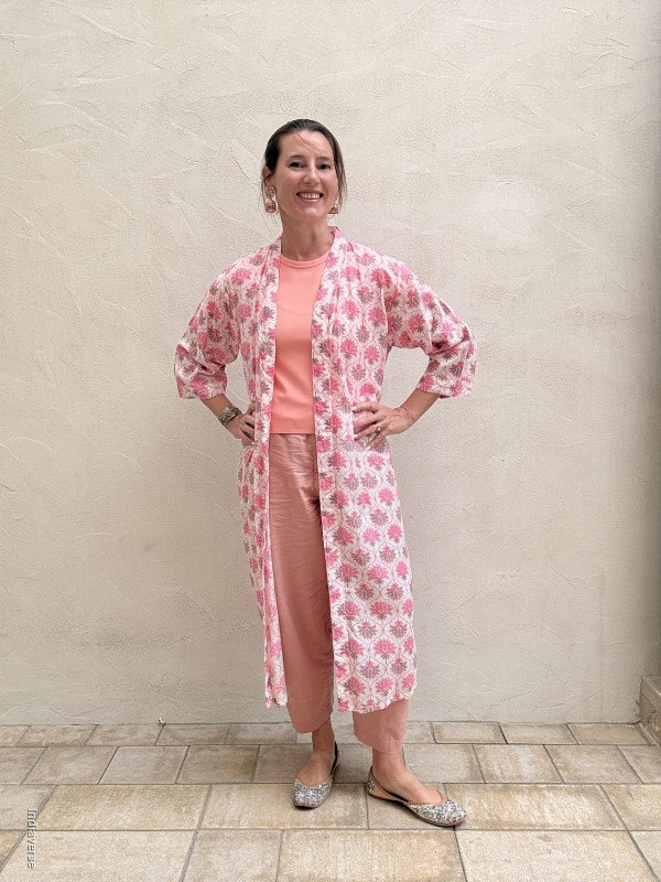 woman wearing a midi size kimono with lotus print and pink pants standing against a beige wall