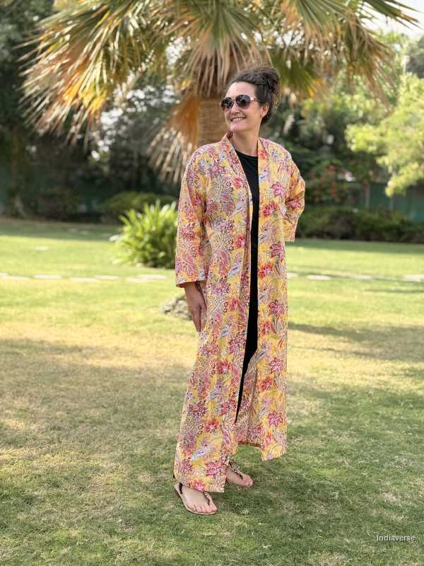 Person wearing a colorful floral kimono-style garment in an outdoor setting with greenery.
