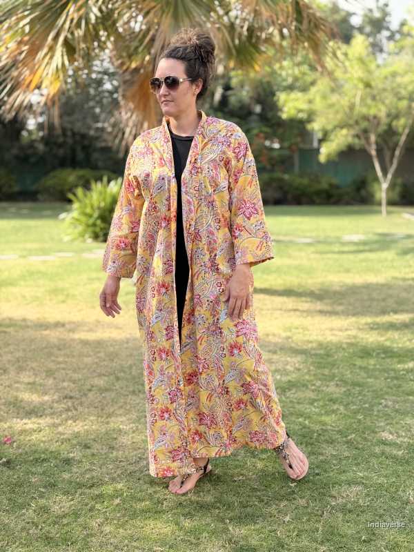 Woman wearing a floral kimono-style garment outdoors on a grassy area with trees in the background.