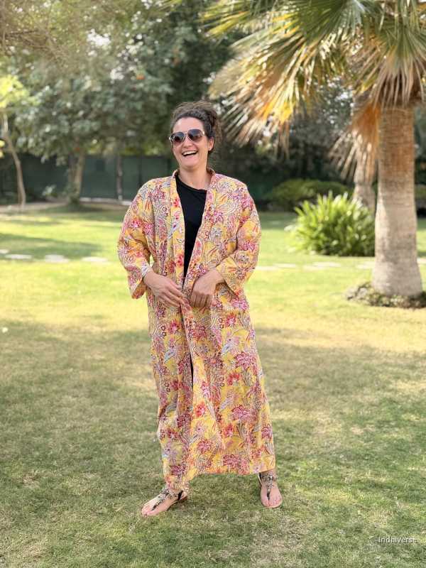 Person wearing a floral dress standing in a garden with trees and grass.