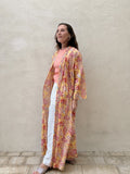 Woman standing in front of a beige wall wearing a long floral robe in yellow with red flowers