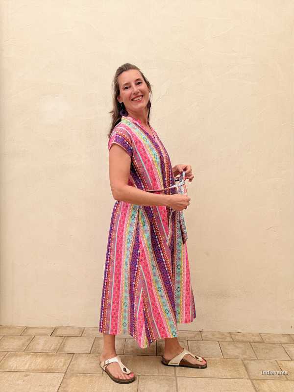 Woman wearing a colorful patterned dress standing against a plain wall.