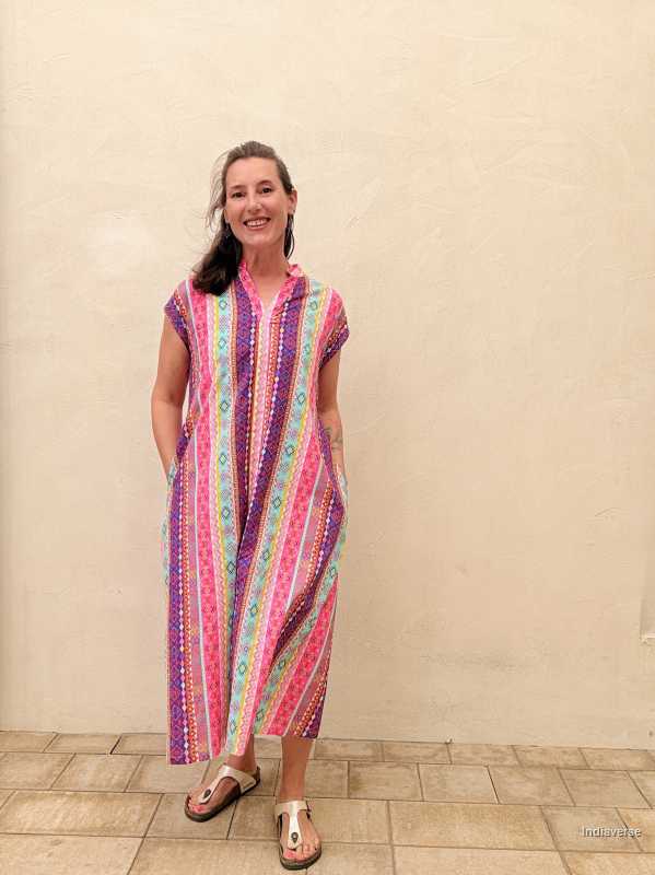 Woman wearing a colorful striped dress standing against a plain wall.