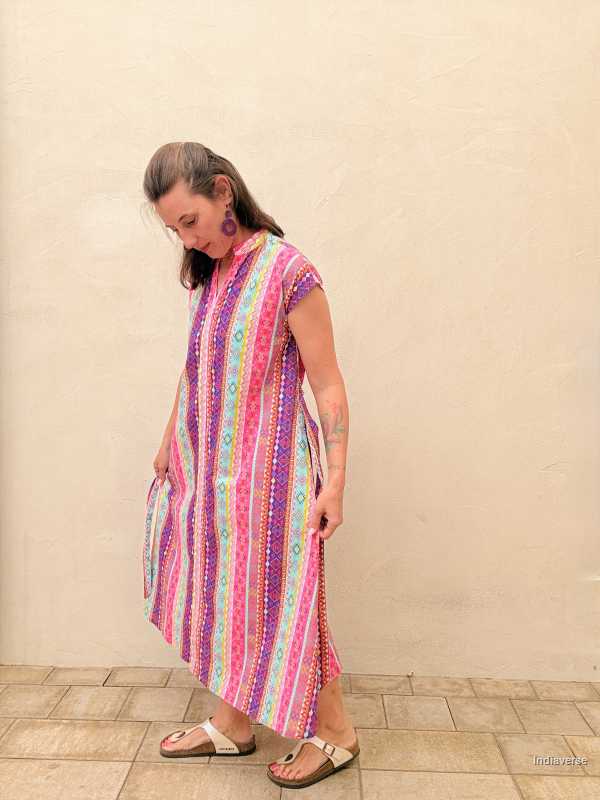 Woman wearing a colorful striped dress against a beige wall.