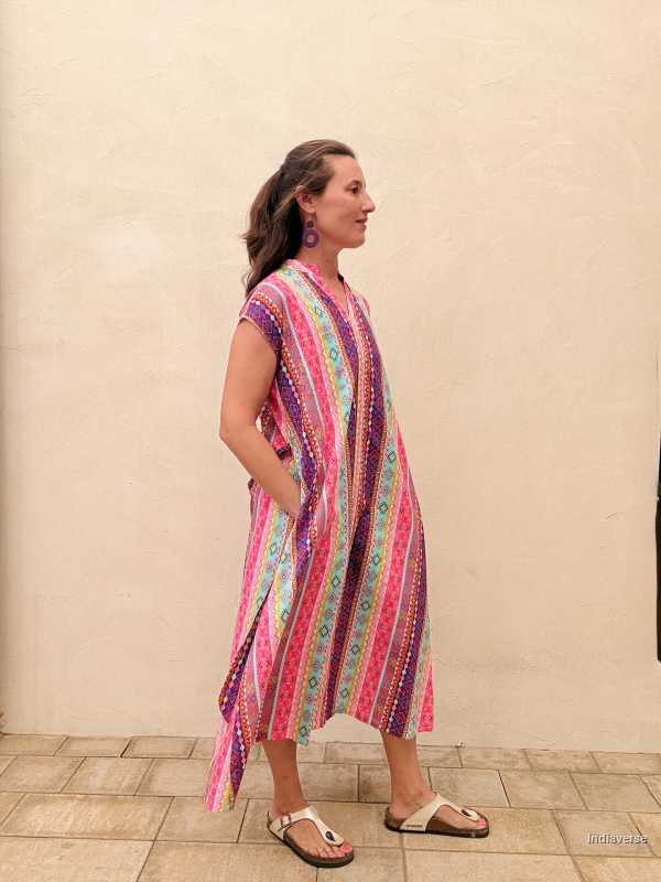 Woman wearing a colorful patterned dress standing against a beige wall.